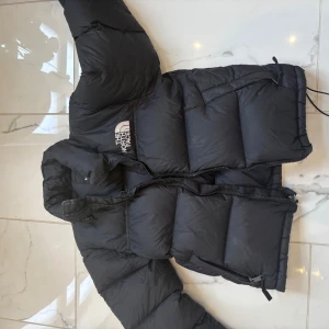 Svart dunjacka från The North Face - Säljer en svart dunjacka från The North Face med klassisk logga på bröstet och ryggen. Jackan har lång ärm, hög krage och dragkedja framtill. Bra skick och kvalité! Använd några gånger! Storlek: S