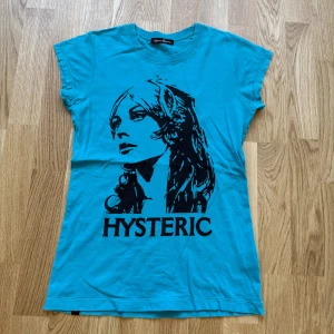 Turkos t-shirt från Hysteric Glamour size s-m - Turkos t-shirt med svart tryck av ett ansikte och texten 'HYSTERIC' på framsidan samt 'DETROIT FOREVER' på ryggen. Klassisk rund hals och normal passform. Perfekt statement-plagg för dig som gillar unika prints.