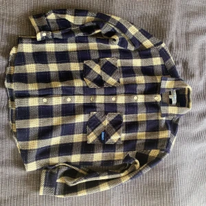 Rutig skjorta från BIGBOY i blått och beige - Säljer en snygg rutig skjorta från Bigboy i blått och beige. Skjortan har långa ärmar,  krage och knäppning framtill. Använd 1 eller 2 gånger så felfritt skick.                  Ge gärna bud också utifrån originalpriset för det är inte hugget i sten. Original priset på skjortan är 1499kr