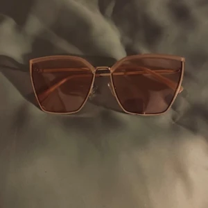 Guldiga solglasögon med bruna glas - Stilrena solglasögon med fyrkantiga, oversized bågar i guldmetall och bruna tonade glas. Perfekta för att lyfta din look med en modern touch och trendig känsla.