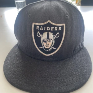 Svart Raiders keps från New Era - Säljer en svart Raiders keps från New Era, modell 59FIFTY. Kepsen har broderad Raiders-logga framtill och NFL-logga baktill. Klassisk rak skärm och normal passform. Perfekt för dig som gillar amerikansk fotboll och streetwear. Jag har växt ut ur den det är därför. Skriv till mig för mer info😁