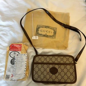 Gucci GG Supreme axelväska - Säljer en klassisk Gucci axelväska i GG Supreme-mönster med bruna skinnkanter och justerbar axelrem. Väskan har ett brunt GG-emblem framtill och levereras med dustbag och originalkartong. Perfekt för dig som gillar tidlös design och lyxiga detaljer.