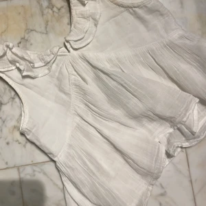 Vit topp me  volang - Säljer denna fina topp åt min lillasyster som vuxit ur den. Köpt på Gina Young. Jätte fin till sommaren. Inga defekter. Skicka gärna prisförslag! Storlek 134/140