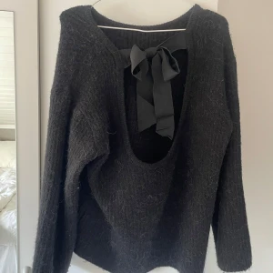 Svart stickad tröja med rosett i ryggen - Mysig svart stickad tröja med lång ärm och stor, djup urringning i ryggen med en rosett. Använd fåtal tillfällen men tyvärr kommer den inte till användning för mig längre.