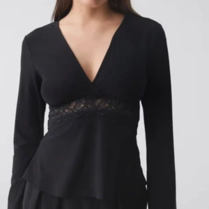 Svart långärmad topp med spetsdetalj - Säljer en svart långärmad topp med v-ringning och spetsdetalj under bysten. Toppen har en feminin och elegant look, perfekt för att lyfta din outfit. Modellen är figurnära och har en mjuk känsla. Den är helt ny och öppnad som ni ser på bilden. Säljer pga jag köpte i fel storlek. 