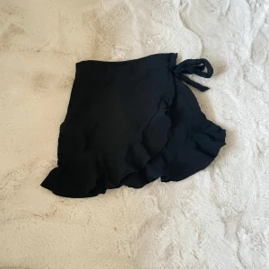 Svart omlottkjol med volang - Säljer en svart kort kjol då den aldrig kommit till användning💓