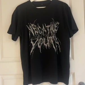 Svart t-shirt med glittrigt tryck - Säljer en svart t-shirt med ett stort glittrigt tryck framtill i silvriga toner. T-shirten har rund hals och korta ärmar, perfekt för en cool och edgy stil. Passar dig som gillar statement-plagg och vill sticka ut.