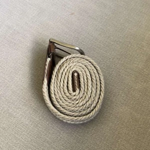 Beige flätat bälte med silverfärgat spänne - Säljer ett snyggt beige flätat bälte med ett klassiskt silverfärgat spänne och bruna skinn-detaljer. Perfekt accessoar för att lyfta din outfit med en stilren touch. Bältet har en mjuk och flexibel känsla tack vare det flätade materialet.