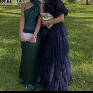 Marinblå långklänning med volanger från By Malina - Säljer en marinblå långklänning från By Malina med flera lager volanger i tyll. Klänningen har kort puffärm och omlott över bysten, går att ha offshoulder också. Är 164 med 7cm klackar, går fortfarande ner mot marken. Bär Xs/s vanligtvis. Använd 1 gång på min bal. Originalpris: 5000kr. Slutsåld överallt. Har ett hål där nere som knappt syns, därmed lågt pris.