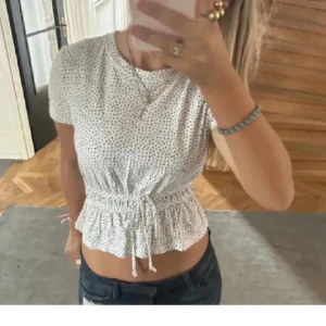 Prickig topp - Vit topp med svarta prickar på med knytning i midjan, jätte fin till våren och sommaren. Tröjan är i toppenskick💓💓