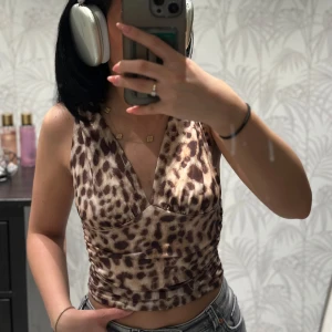 Leopardmönstrad topp med v-ringning - Säljer en croppad topp med leopardmönster och djup v-ringning både fram och bak. Toppen har breda axelband som kan bäras på två olika sätt. Den är figurnära med rynkade detaljer i midjan. 