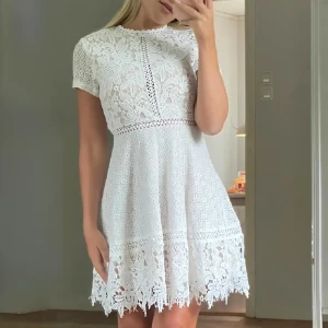 Helt ny! Vit spetsklänning  - Superfin, helt ny, vit spetsklänning med korta ärmar och hög hals. Klänningen har vackra spetsdetaljer, markerad midja och en lätt utsvängd kjol med dekorativ kant nertill. Perfekt för somriga tillfällen eller student 💗 Storlek XS | Köparen betalar frakt 