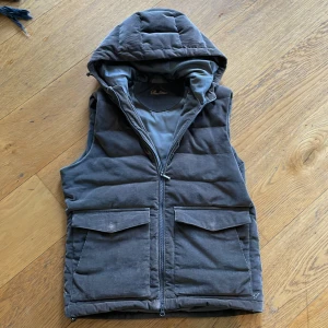 Grå quiltad manchesterväst med huva - Säljer en grå stenström väst i manchester med huva och dragkedja framtill. Västen har två stora fickor. Snygg och praktisk för en sen sommarkväll.