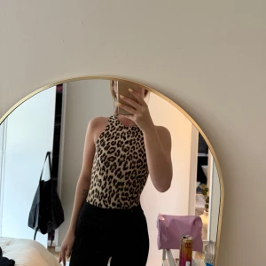 Leopardmönstrad ärmlös body - Säljer en snygg ärmlös body med leopardmönster. Toppen har hög hals och är figurnära, perfekt att styla med både jeans och kjol. Mjuk och stretchig känsla.