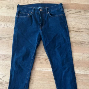 Mörkblå jeansbyxor - Säljer ett par klassiska mörkblå jeansbyxor med fem fickor och knappgylf. Byxorna har raka ben och normal passform, perfekta till vardags. Snygga kontrastsömmar och tidlös design.