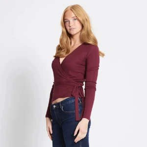 Vinröd omlottopp med knyt - Vinröd omlottopp med lång ärm och knyt i sidan. Djup v-ringning och figurnära passform🍾🥂🌸. Perfekt till jeans eller kjol för en snygg och enkel look. Lånad bild💗