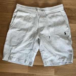 Ralph Lauren shorts - Snygga ljusgrå shorts från Polo Ralph Lauren med dragsko i midjan och två sidofickor. Klassisk logga broderad på vänster ben. Perfekta för sommardagar och avslappnade tillfällen.