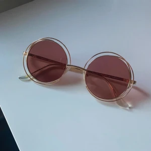 Runda Pilgrim solglasögon i rosa och guld - Äkta Pilgrim solglasögon med rosa-rött glas och guld detaljer. Köptes för 400kr några år sedan! Inga defekter förekommer  