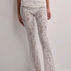 Vita spetsbyxor med blommigt mönster - Säljer ett par vita byxor i spets med blommigt mönster. Byxorna är genomskinliga och har en bootcut passform med låg midja. De är från Nelly förra säsongen💕.