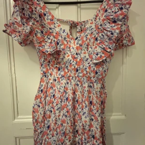 By Malina klänning  - Oanvänd By Malina klänning. Söt kortklänning med blommigt mönster i rosa, blått och vitt. Klänningen har volangdetaljer vid axlar och byst, v-ringning och knytning i ryggen. Perfekt för sommarens alla tillfällen. Jätte bra skick