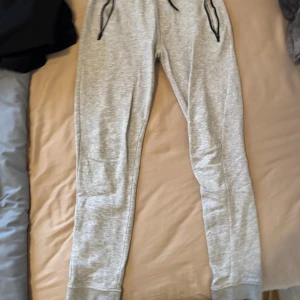 Grå mjukisbyxor från SOC - Säljer ett par ljusgrå mjukisbyxor från SOC med svarta dragsnören i midjan och muddar vid bensluten. Perfekta för chill eller träning. Mjukt material och bekväm passform.