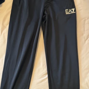 2st Svarta mjukisbyxor från EA7 Emporio Armani - Svarta mjukisbyxor från EA7 Emporio Armani med logga på vänster lår. Byxorna har elastisk midja och raka ben. Perfekta för en avslappnad stil och passar bra till vardags eller träning.