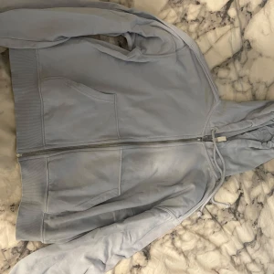 Ljusblå hoodie med dragkedja - Mysig ljusblå hoodie med dragkedja och huva. Jackan har två fickor framtill och är fodrad med mjuk fleece på insidan. Perfekt för kyliga dagar och enkel att matcha med olika outfits.