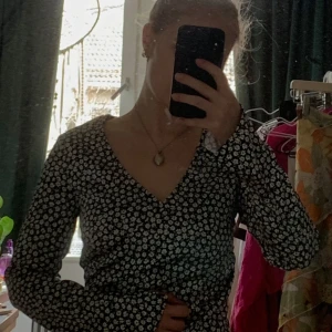 Svart blommig topp från C&A - En blommigt mönstrad topp som är lite silkig från H&M i storlek S. Toppen har lite utsvängda ärmar, v-ringning och är figurnära i modellen. 
