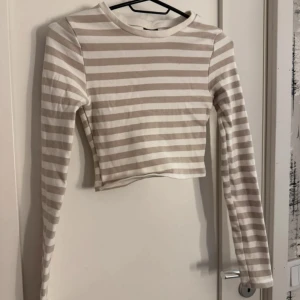 Beige och vit randig croppad tröja från Gina Tricot - Säljer en croppad långärmad tröja från Gina Tricot i storlek XS. Tröjan är beige och vit med horisontella ränder och har en tight passform. Perfekt för en trendig och avslappnad look.