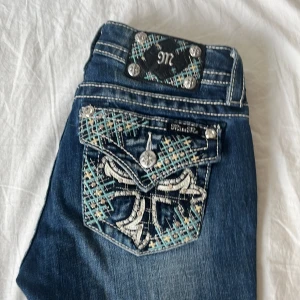 Fett snygga trendiga jeans från Miss Me  - Snygga blå jeans från Miss Me med unika broderade fickor. Säljer då de var lite för stora för mig och är därför aldrig använda. Mått: midjemått är 37 cm, innerbenslängd är 84 cm, hela byxor är 106 cm och 20 cm i midjehöjd.                                                               Det står på lappen att det är bootcut och mid-rise men skulle säga att de är low-rise. Ett riktigt måste i garderoben och kan fixa vilken outfit som helst. Perfekt nu till våren. Skriv vid minsta fråga? 💕🌼🌞