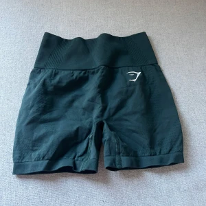 Mörkgröna shorts från Gymshark - Säljer ett par svarta shorts från Gymshark med låg midja och ribbad detalj. Perfekta för träning med en bekväm passform och stilren design.