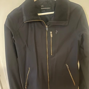 Svart jacka från Peak Performance - Snygg svart jacka från Peak Performance med dragkedja framtill och två fickor med dragkedjor. Perfekt för kyligare dagar med sin stilrena design och praktiska detaljer.