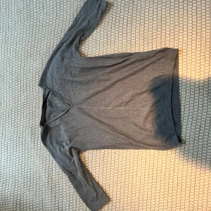 Grå långärmad tröja - Säljer en stilren grå långärmad tröja med v-ringning. Perfekt för en avslappnad look. Tröjan har en normal passform och är tillverkad i ett mjukt material.