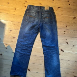 Blå washed jeans från Nudie Jeans - Säljer ett par snygga blå jeans från Nudie jeans med en sjuuuk wash🦕 Jeansen är tillverkade i slitstarkt denim och är bara använda i en vecka👔Nypris: 1600💰De är i storlek 29/30 men sitter som 30/30😶‍🌫️ Perfekta för en avslappnad stil🐦‍🔥Hör av dig vid frågor!🙏