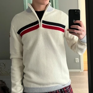 Vit skidtröja/fleece från Swix - ANVÄND 1-2 ggr. NYPRIS: 1799 kr. Säljer en stilren vit tröja från Swix med dragkedja och ränder i blått och rött över bröstet. Tröjan har grå ribbade muddar vid ärmslut och nederkant samt en hög krage. Skitsnygg på afterskin eller en kylig dag.  