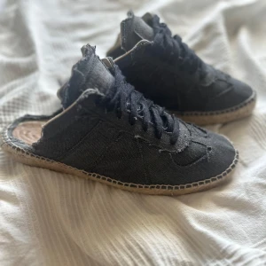 RAW TRIM EDGE ESPADRILLOS  - Unika svarta sneakers från Maison Margiela i jeansmaterial med snörning och rund tå. Skorna har en distinkt design med synliga sömmar och en espadrille-liknande sula. Perfekta för dig som vill ha något annorlunda och stilrent. Storlek 44 suveränt skick är mest ute för byten 
