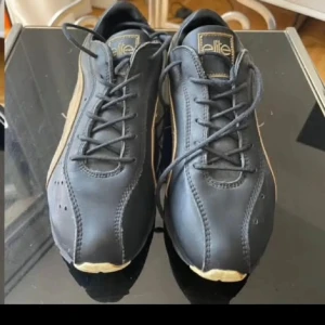 Svarta sneakers från Elite 37 - Snygga svarta sneakers från Elite med beige detaljer och snörning. Skorna har en rund tå och en unik sula med mönster för extra grepp. Perfekta för en stilren look.