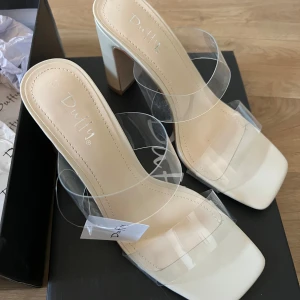 Beige klackskor från Duffy - Snygga beige klackskor från Duffy med transparenta remmar och fyrkantig tå. Aldrig använda, prislapp kvar. Storlek 37