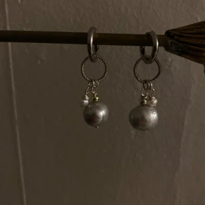 Silverfärgade örhängen med pärlor - Snygga silverfärgade örhängen med hängande pärlor. De har en vriden ringdesign och små detaljer som ger en elegant touch. Perfekta för att lyfta vilken outfit som helst. Allt är i äkta silver förutom ”hopsen” som är i rostfritt stål. Äkta sötvattens pärlor 