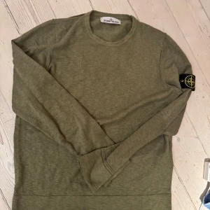 Olivgrön tröja från Stone Island - Säljer en stilren olivgrön tröja från Stone Island. Tröjan har långa ärmar och en rund halsringning. Den ikoniska Stone Island-loggan sitter på ärmen. Perfekt för en avslappnad och trendig look.