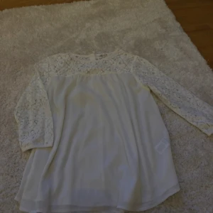 Vit blus med spetsdetaljer - Säljer en elegant vit blus från Kappahl med vackra spetsdetaljer på ärmar och överdel. Blusen har trekvartsärmar och en luftig passform, perfekt för en stilren look. Passar bra till både jeans och kjol. Storlek 164, motsvarar XS/S