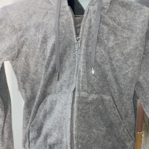 Grå hoodie från Juicy Couture - Säljer en snygg grå hoodie från Juicy Couture med dragkedja och huva. Perfekt för en avslappnad stil. Den är inte i ny skick men den är i ett bra skick. Nypris ligger på runt 800, men jag säljer den för 250 kr för de är väldigt bra skick för priset. Den är i storlek XS.