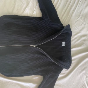 Svart fullzip från sams pris kan diskuteras - Snygg svart ribbad tröja med dragkedja framtill. Perfekt för kyligare dagar med sin höga krage och långa ärmar. En stilren och mångsidig tröja som passar till det mesta.