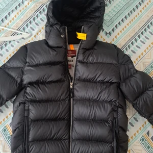 Svart pufferjacka från Parajumpers - Säljer en svart pufferjacka från Parajumpers, modell Sheen Pharrell. Jackan har en dragkedja framtill och en huva för extra värme.