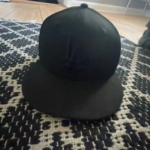 Svart keps från New Era - Säljer en stilren svart keps från New Era, modell 59FIFTY. Kepsen har en broderad logga framtill och MLB-logga baktill. Perfekt för att komplettera din streetwear-look. Pris kan diskuteras