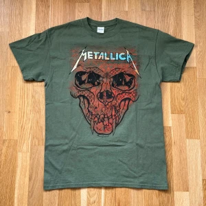 Metallica World Wired Tour 2019 Grön T-Shirt - Metallica T-Shirt med tryck både fram och back i färgen grön. Från deras tour 2019 ”World Wire”. Storlek: M, Armhåla till Armhåla: 48 cm, Längd: 70 cm, Axel till Armöppning: 16 cm.  Material: 100% Cotton.