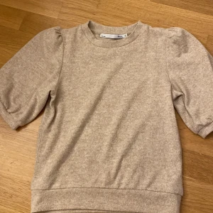 Stickad t- shirt från lager 157 - Fin beige stickad t- shirt från lager 157. Tröjan har puffiga armar. Storlek S. 🤍