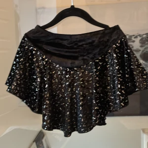 Svart glittrig konståkningskjol från Jerry's Skating World - Säljer en svart glittrig kjol från Jerry's Skating World. Kjolen har en volangdetalj och är tillverkad i polyester och spandex för en stretchig passform. Perfekt för att glittra på isen eller andra festliga tillfällen. ✨