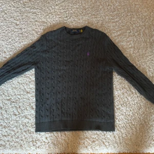 Stickad Ralph lauren tröja - Säljer en stickad Ralph lauren tröja i färgen mörk grå, den är unik med den lila loggan som gör det till en skit snygg tröja. Den grå färgen gör den enkle att matcha med.Pris går att diskutera vid snabb affär😉
