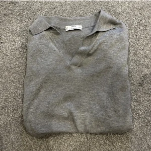 Grå pikétröja från MNG - Säljer en stilren grå pikétröja från MNG i en mjuk silkeblandning. Tröjan har en klassisk krage och v-ringning, perfekt för en avslappnad men ändå snygg look. Passar bra till både jeans och shorts. Perfekt för våren men också sommarn. Bra skick!!